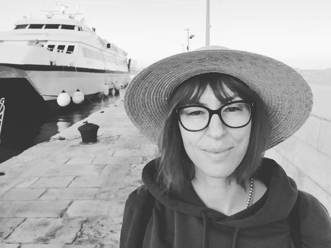 Person wearing a wide-brimmed hat and hoodie standing at a harbor with a large ship in the background.