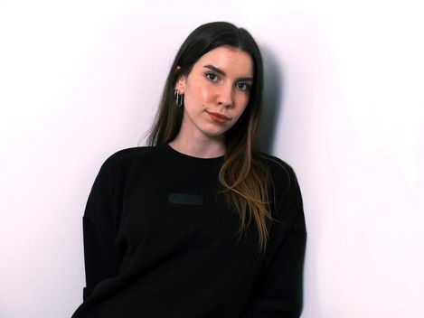 Woman with long hair wearing a black sweater and earrings against a white background.