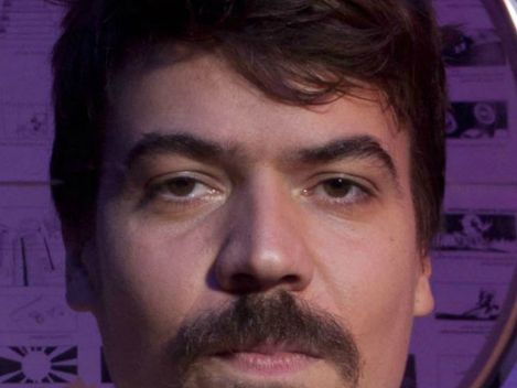 Man reflecting messy hair with purple background and wall decorations.