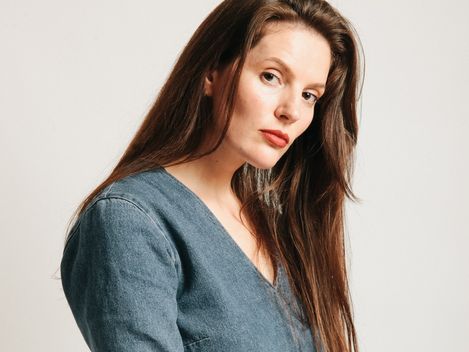 Person with long brown hair wearing a V-neck denim sweater against a light background.