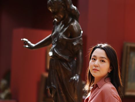 portrait of a woman wearing a light pink blouse in a museum