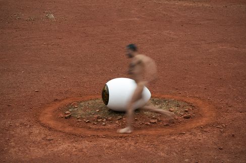 Blurred image of a naked man running past a large white eye-shaped object on red ground