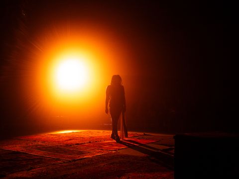 The silhouette of a person against a glowing orange light on a dark stage.