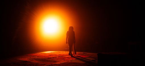 The silhouette of a person against a glowing orange light on a dark stage.