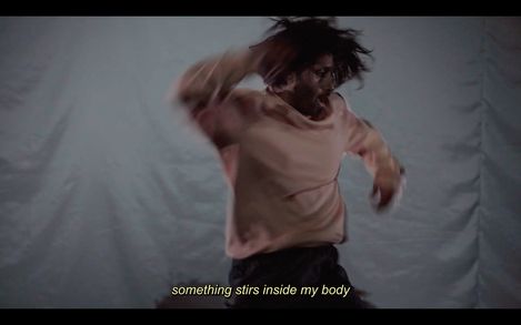 Person with long hair and sweater in motion against a plain background with subtitle "something stirs inside my body".