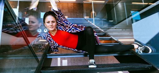 Frau in rotem Oberteil und gemustertem Cardigan liegt seitlich auf einer Treppe und stützt sich mit verschränkten Armen an das Geländer