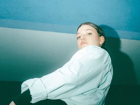 Junge Frau in weißem Hemd vor blauem und weißem Hintergrund, von unten fotografiert