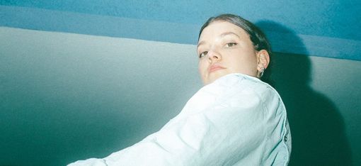 Junge Frau in weißem Hemd vor blauem und weißem Hintergrund, von unten fotografiert
