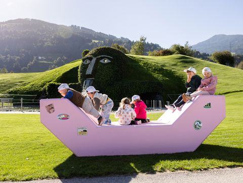 Kinder spielen auf einem rosa Enzi vor dem begrünten Riesen der Swarovski Kristallwelten in Wattens.