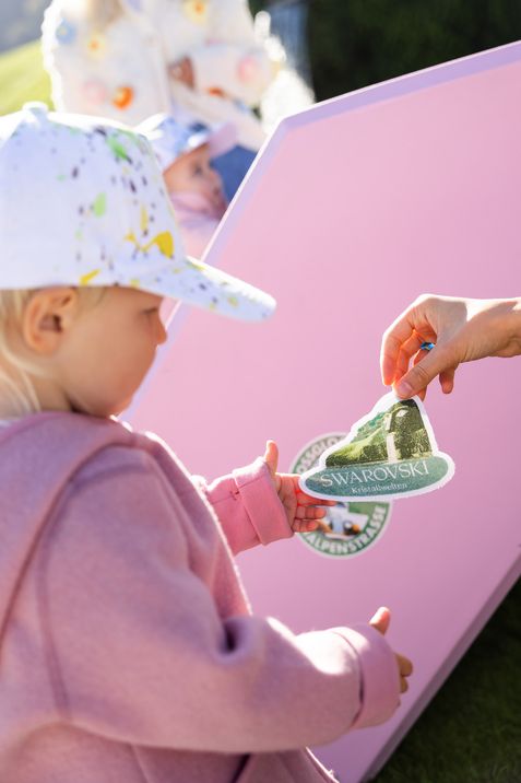 Ein Kind bringt einen Swarovski-Kristallwelten-Sticker auf einem rosa Enzi an.
