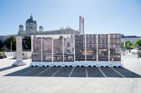 Große Außeninstallation mit mehreren nebeneinander stehenden Tafeln, die historische Fassadenabbildungen zeigen, im hellen Stadtplatz mit klassischem Gebäude im Hintergrund