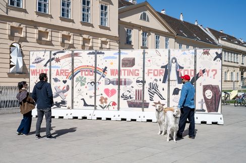 Menschen mit Hund betrachten eine große bemalte Wand mit der Aufschrift 'WHAT ARE YOU WAITING FOR TODAY' und verschiedenen Zeichnungen in einem städtischen Umfeld.