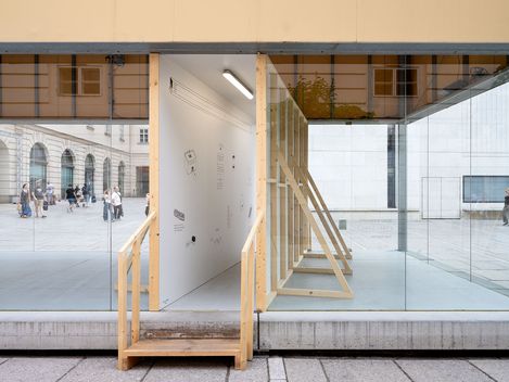 Holztreppe führt in einen gläsernen Raum mit weißen Wänden und minimalistischer Einrichtung in einem städtischen Umfeld