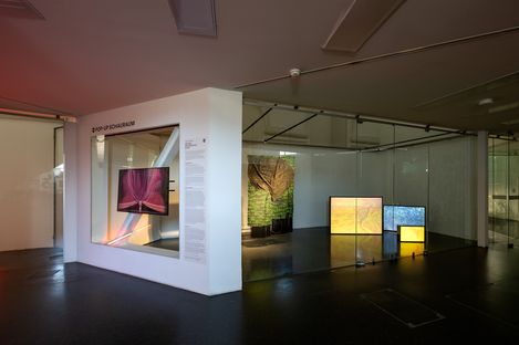 Innenraum einer Ausstellung mit mehreren beleuchteten Bildschirmen und einer weißen Wand mit Text und dem Schriftzug '2. POP-UP SCHAU RAUM'