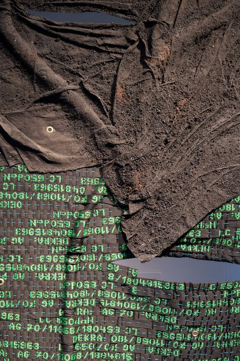 Nahaufnahme von zerknittertem, schmutzigem Stoff mit aufgedruckten grünen Zahlen und Buchstaben in einer Matrix-ähnlichen Anordnung