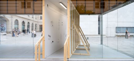 Holztreppe führt in einen gläsernen Raum mit weißen Wänden und minimalistischer Einrichtung in einem städtischen Umfeld