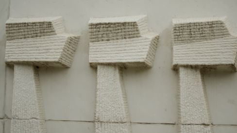 Drei grob behauene Steinkreuze an einer hellen Wand.