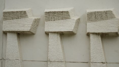 Drei grob behauene Steinkreuze an einer hellen Wand.