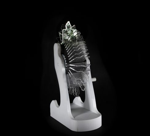 Sculpture with multiple transparent layered acrylic plates on a white base against a black background.