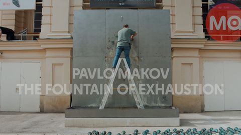 Installation setup of “The Fountain of Exhaustion” by Pavlo Makov at MuseumsQuartier Vienna, with a person standing on a ladder in front of the metal structure.