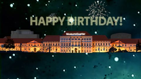 Beleuchtetes MuseumsQuartier-Gebäude bei Nacht mit Feuerwerk und Schriftzug 'HAPPY BIRTHDAY!' am Himmel