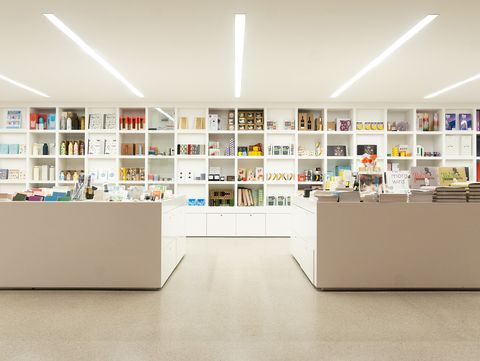 Symmetrical wide view of a modern museum shop with white furniture, shelving and a diverse product range.