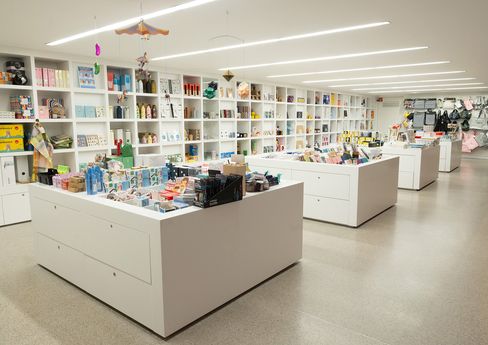 Bright museum shop with white shelving and central display tables filled with books, design objects and gift items.