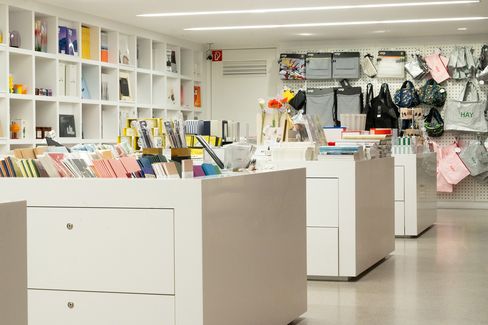 Display tables in the museum shop featuring stationery, books and design accessories in front of a shelving wall.