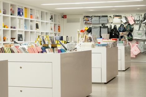 Display tables in the museum shop featuring stationery, books and design accessories in front of a shelving wall.