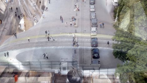 Vogelperspektive auf eine belebte Kreuzung mit Fußgängern, parkenden Autos und Bäumen am Straßenrand.