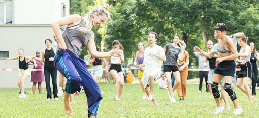 Woman with long blonde hair dancing barefoot on grass in front of a group of people following or watching her