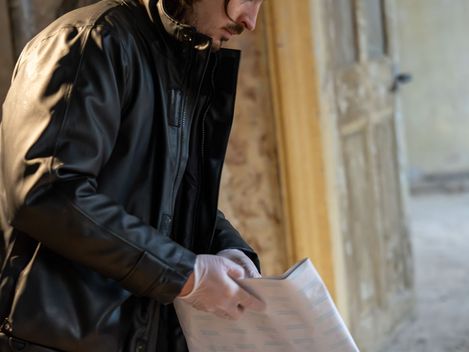 Person with medium-length hair wearing a black leather jacket stands at a table holding an open booklet.