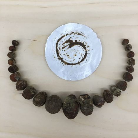 Semi-circle of irregular earthy stones on a light surface with a crumpled white paper circle in the center showing a spiral pattern made of soil.