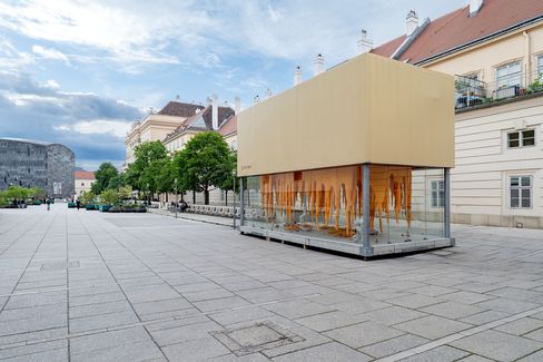Three people stand outside an art gallery window displaying orange, melting-like sculptures labeled "ART BOX" on a city street.