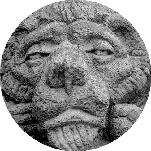 Schwarz-weißes, kreisförmiges Detail einer Steinskulptur, Nahaufnahme des Gesichts mit geschlossenen Augen und herausgestreckter Zunge.