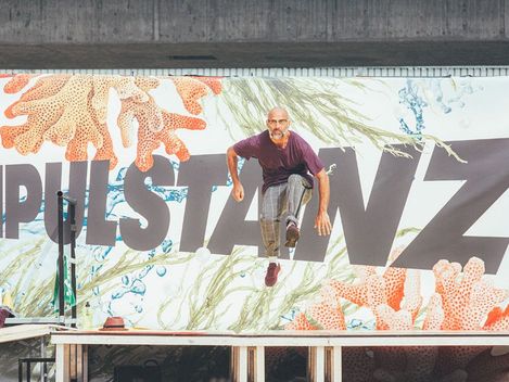 Mann in Bewegung springt vor einer Wand mit großem Schriftzug und Meeresmuster