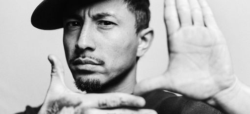 Man wearing a baseball cap holds his hands in front of his face, one hand flat toward the camera, the other horizontal in front.