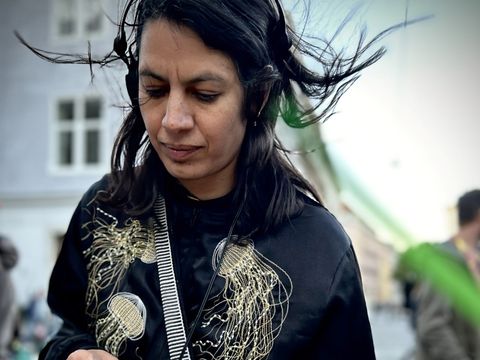 Person with long hair wearing headphones standing in front of a turntable outdoors