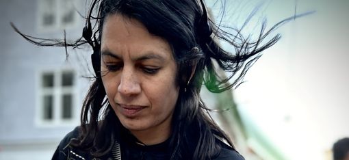 Person with long hair wearing headphones standing in front of a turntable outdoors