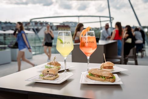 Two KATTUS drinks and several filled rolls on plates in an outdoor terrace area, with guests in the background.
