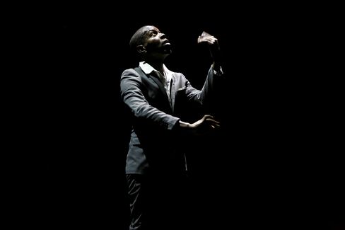 Man in suit raising a fist and looking upward against a black background.