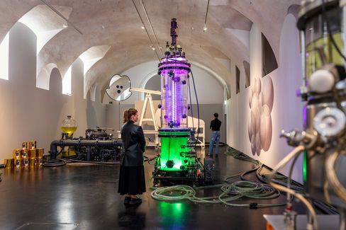 Person stands in front of a large cylindrical illuminated installation in a vaulted ceiling room.