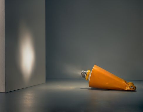 Crushed orange tube lying on gray floor in front of gray wall with light spot on the wall.