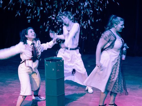 Three women dressed in white are dancing. They seem to be celebrating something: confetti is flying, and they are holding glasses in their hands.