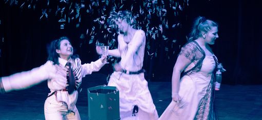 Three women dressed in white are dancing. They seem to be celebrating something: confetti is flying, and they are holding glasses in their hands.