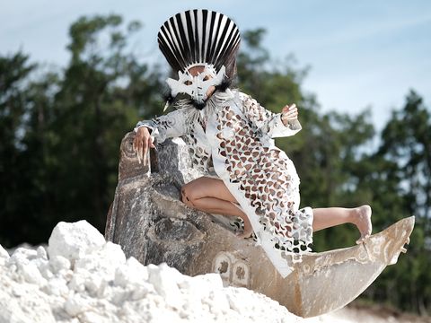 A dancer in a white costume and wearing a mask is sitting on a rock