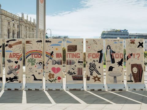 Pillars displaying colored-pencil drawings on both sides stand against an urban backdrop.