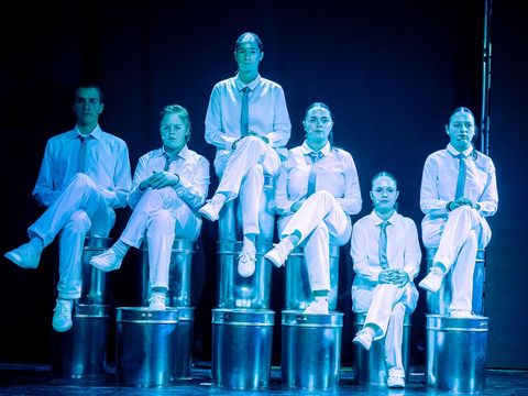 Six people are sitting on stacked metal buckets, dressed in white costumes.