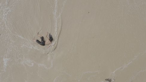 Aerial view of a person moving in shallow water on a sandy surface creating a wave.