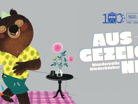 Das Bild zeigt einen Ausschnitt einer Bilderbuchillustration von Marc Boutavant. Zu sehen ist ein Bär mit einem gelben Hemd und einer kurzen grünen Hose, der vor einem Tischchen auf einem rosakarierten Teppich steht. Der Bär trägt einen kleinen Partyhut und sieht genießerisch drein.